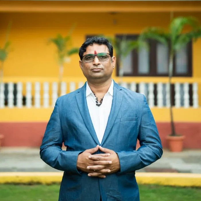 Prakash Shastry in a blue blazer, hands clasped, outside a yellow building