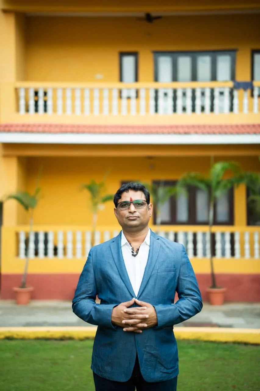 Prakash Shastry Somanchi in a blue blazer with his hands together, standing on a lawn