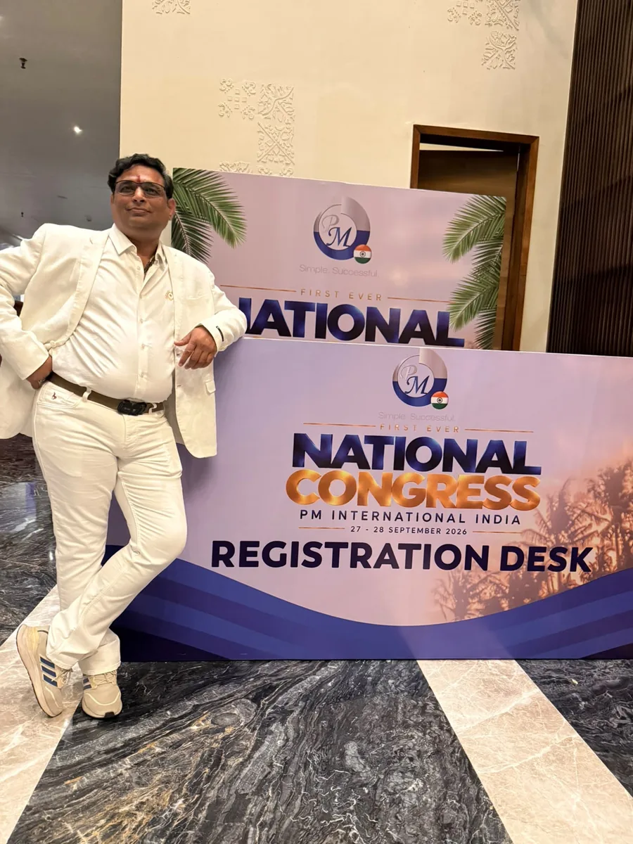 Prakash Shastry Somanchi in white, standing beside the PM International India National Congress registration desk sign