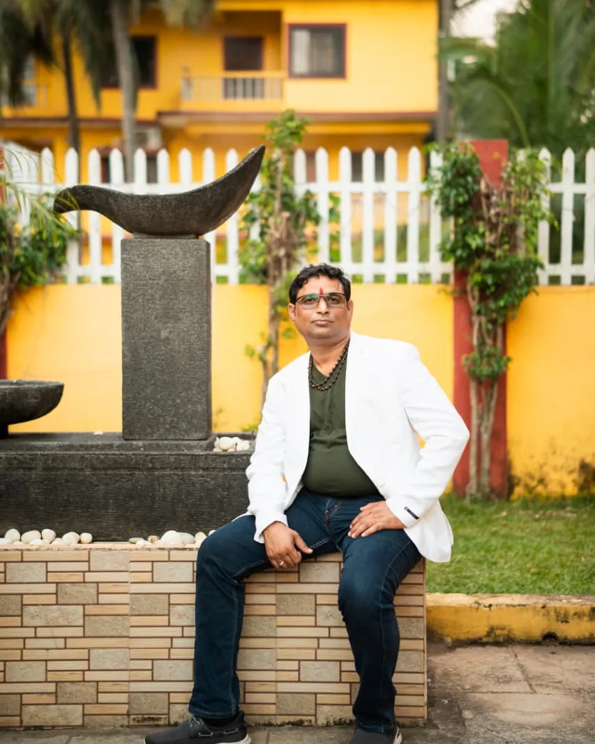 Prakash Shastry in a white blazer, seated beside a garden fountain